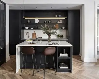 Una cocina de galera negra con paredes y encimeras blancas e iluminación llamativa sobre una barra de desayuno.
