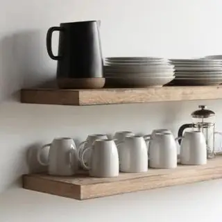 Tazas y jarras pequeñas alineadas en la misma dirección sobre un estante flotante de madera