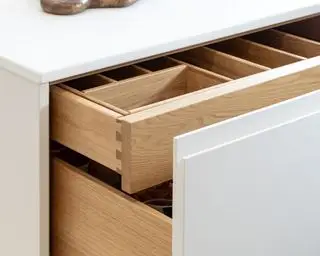 Gabinetes de cocina blancos que muestran un cajón que se abre sobre una unidad base blanca con una sección de almacenamiento extraíble oculta para cubiertos