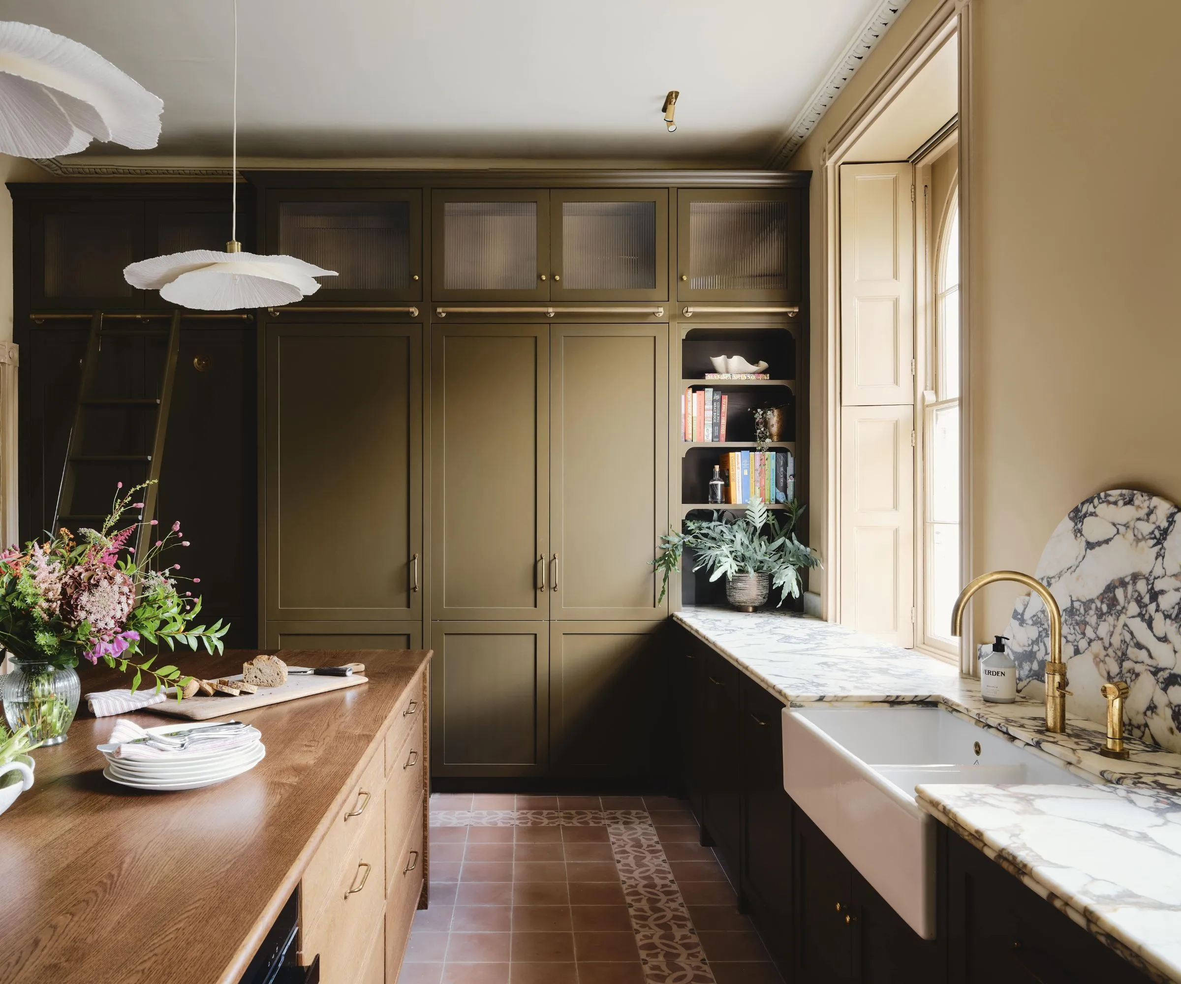 Una calda cucina country con mobili verdi, ripiani in marmo con isola in legno e un lavello in porcellana' loading='lazy' title=