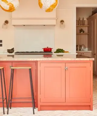 Cucina Shaker con isola corallo, pareti rosa, sgabello bar, pavimento piastrellato, piano in marmo