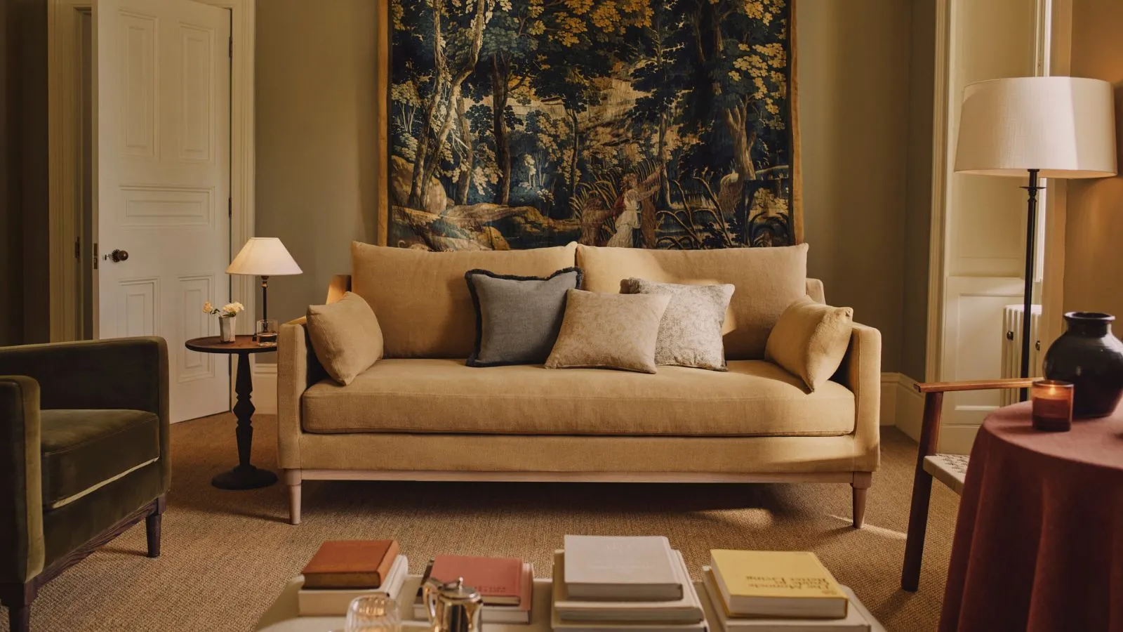 סלון צהוב עם ספה צהובה חמאה ושטיח גדול תלוי מאחור מעוצב עם כורסת קטיפה ירוקה ושולחנות קטנים עם מנורות' loading='lazy' title=