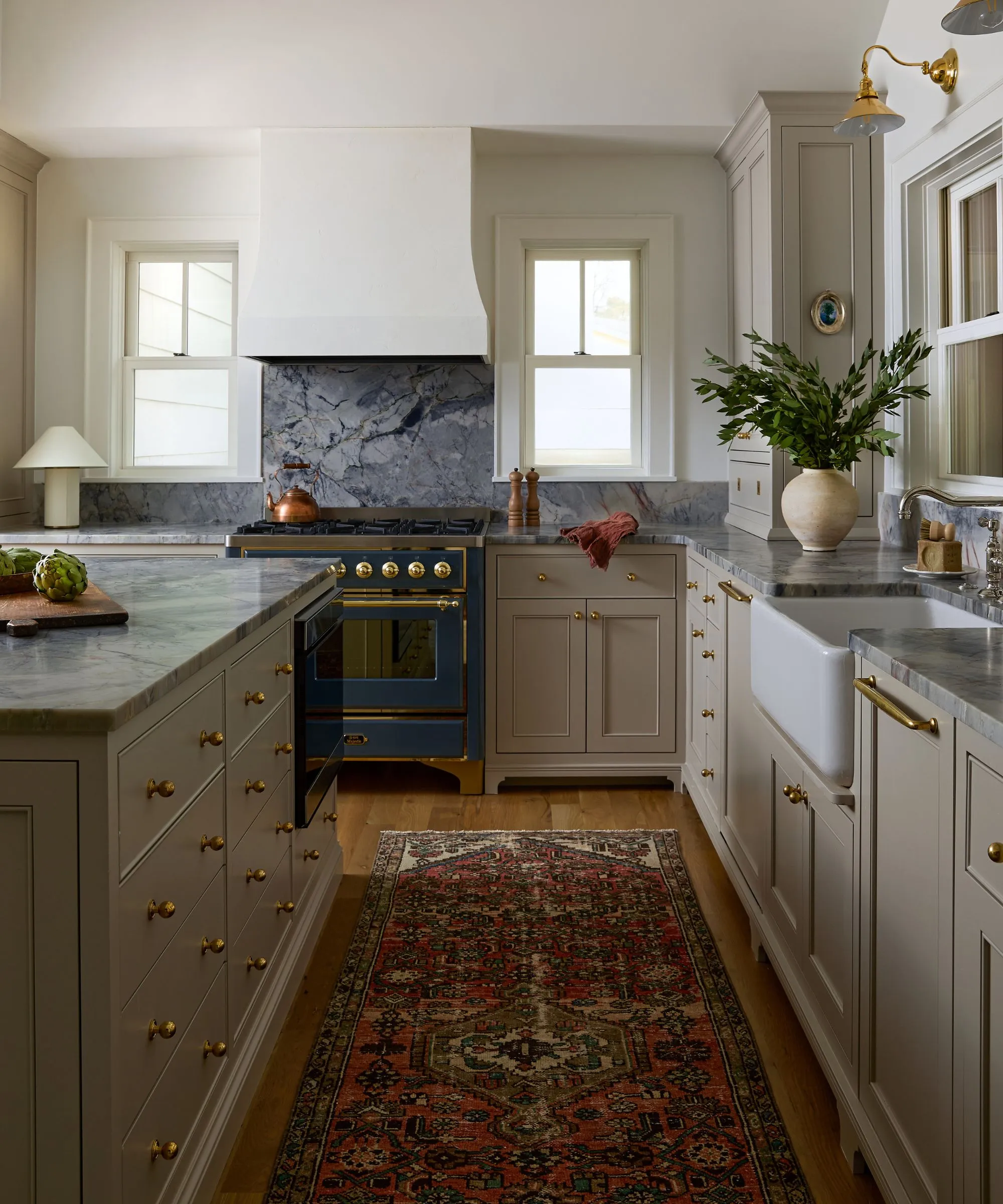 מטבח נייטרלי ארצי עם חלונות גדולים היוצאים לנוף של שפת האגם, קולט אדים גדול מגבס ומשטחי שיש כחול' loading='lazy' title=