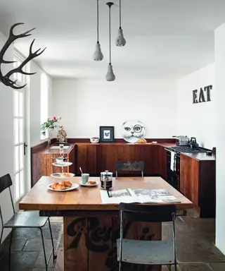Uma cozinha com armários em azul profundo, acessórios de latão e uma área de estar com janela baixa