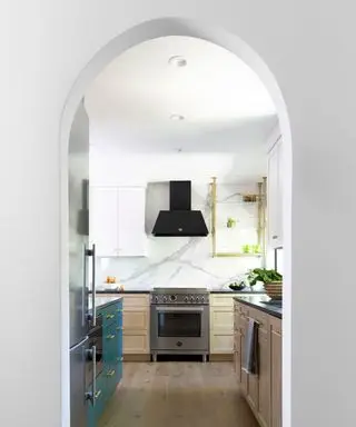 Cocina de galera vista a través de un arco con gabinetes azules y de madera