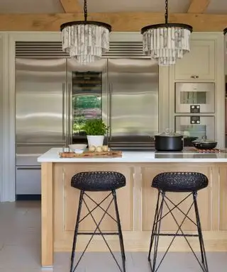 Una cocina de madera clara con una pequeña península con taburetes negros y encimeras de mármol blanco.