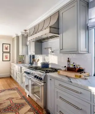 Cocina gris claro con suelo de madera y alfombra vintage.