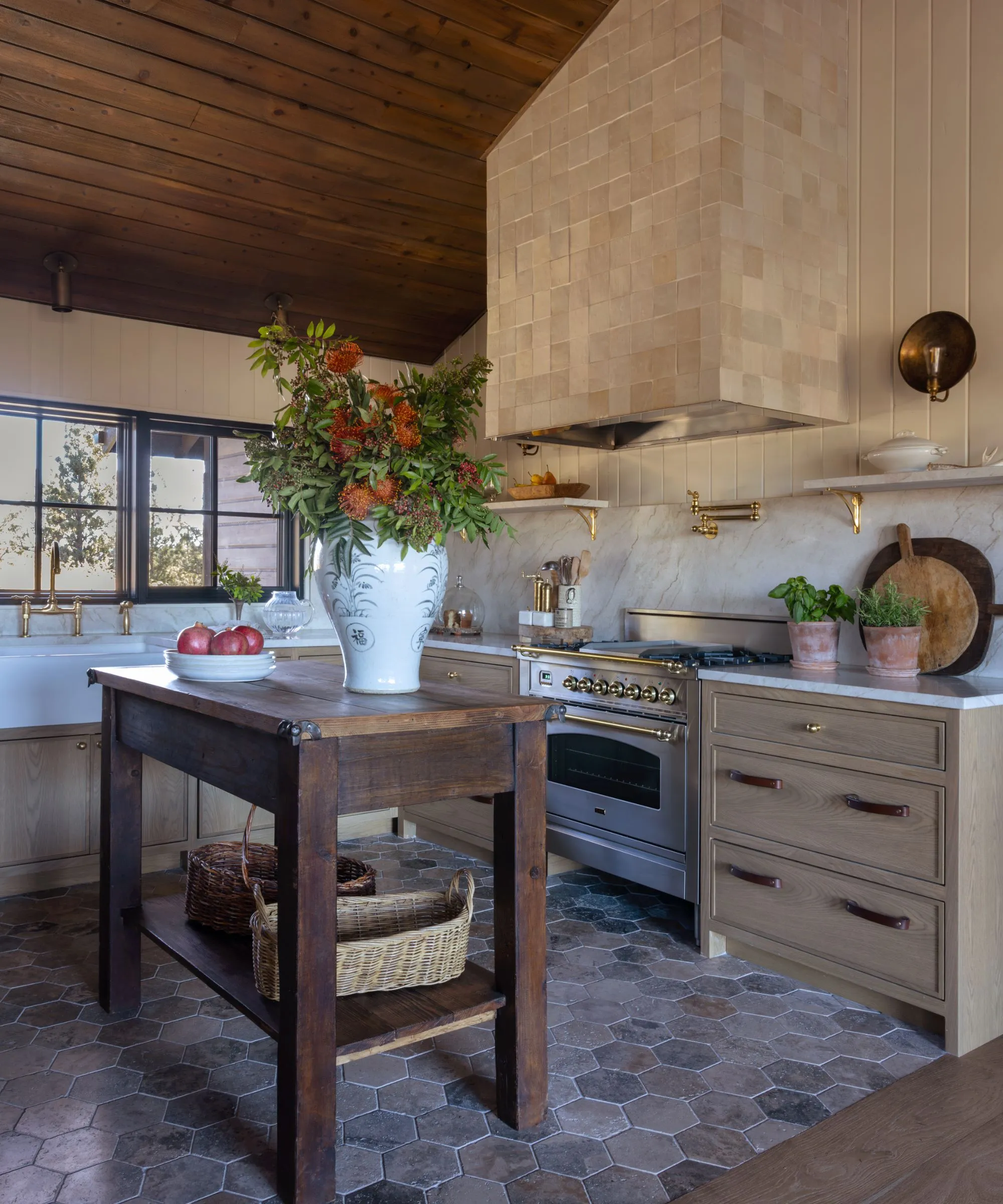 Eine warme, rustikale Küche mit Holzschränken, einer Rückwand aus Marmor und strukturierten quadratischen Fliesen, die das Kochfeld bedecken' loading='lazy' title=