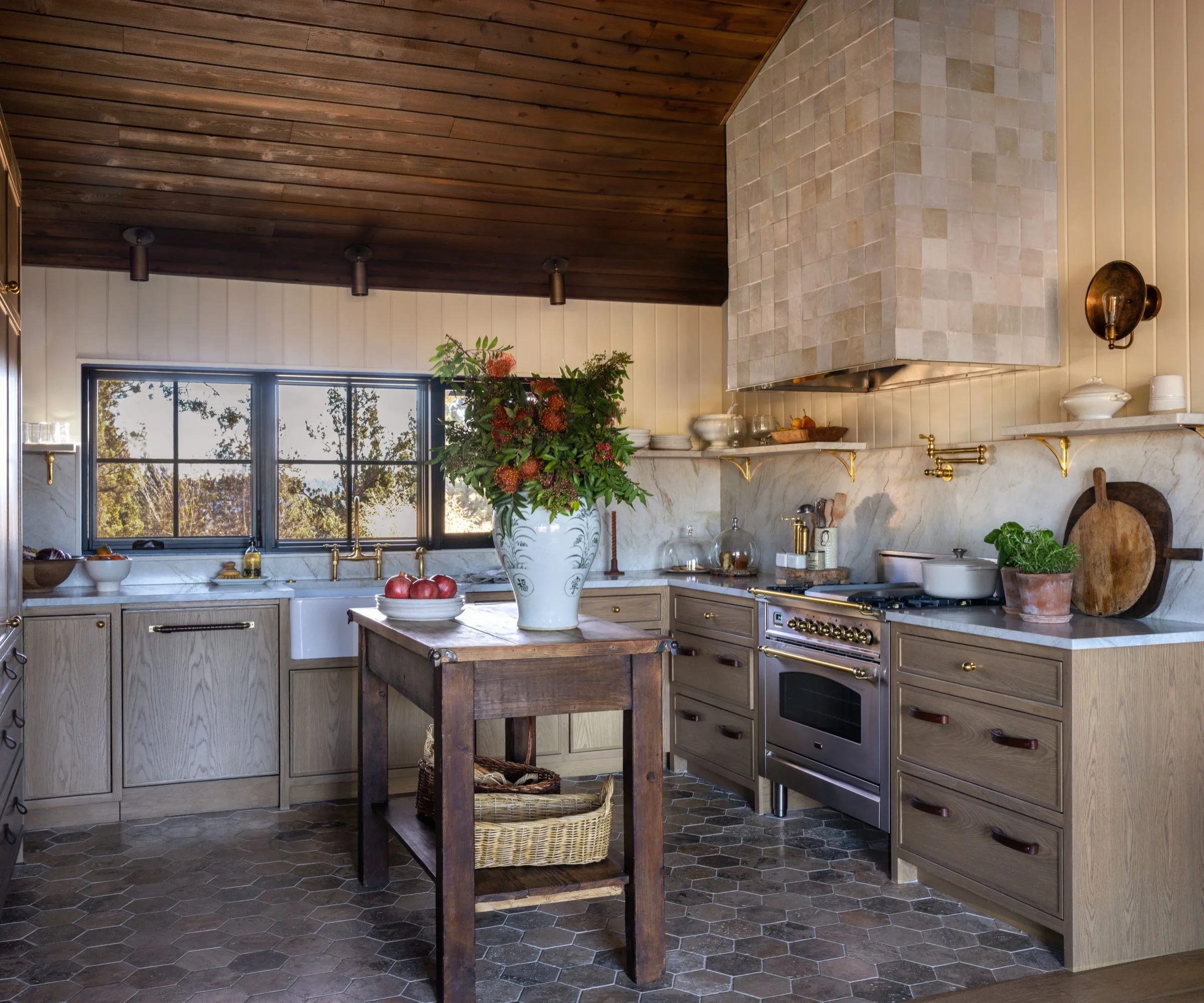 Eine detaillierte Ansicht des Küchenarbeitsplatzes mit einem schweren Bauernwaschbecken aus Marmor, unlackierten Messingbeschlägen und einer integrierten Rückwand aus Marmor. Die Szene zeigt einen Gasherd unter einer minimalistisch verputzten Dunstabzugshaube' loading='lazy' title=