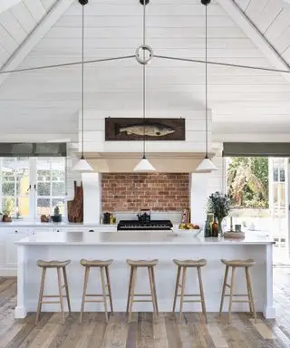 Cocina blanca con revestimiento y techo abovedado e isla con taburetes en una nueva construcción costera de Cornualles