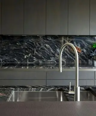 Primer plano de una encimera de mármol blanco y negro con fregadero de metal y grifo mezclador y armarios de cocina de color gris oscuro.