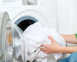 Mujer sacando ropa blanca de una lavadora.