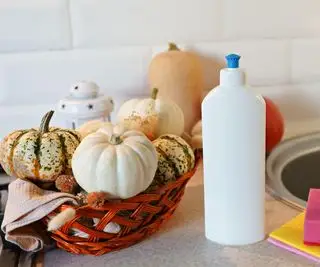 Ein Korb mit Kürbissen neben einer Flasche Seife und Schwämmen in einer Küche