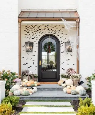 Halloween-Türdeko-Ideen mit hellen Kürbissen auf dem Boden und schwarzen Fledermäusen an den Häusern