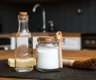 bottiglia di aceto bianco accanto a un contenitore di zucchero e uno spazzolone