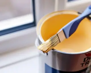 lata de tinta amarela e pincel pela janela