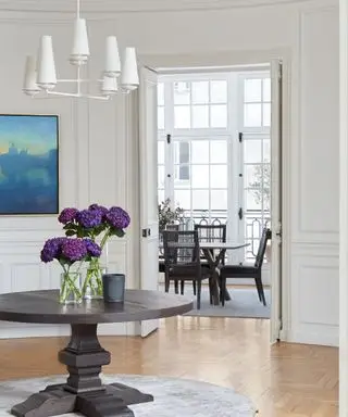 corredor com painéis brancos com mesa redonda e vista para a sala de jantar