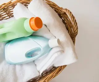 Un panier à linge avec des draps pliés et des bouteilles de lessive