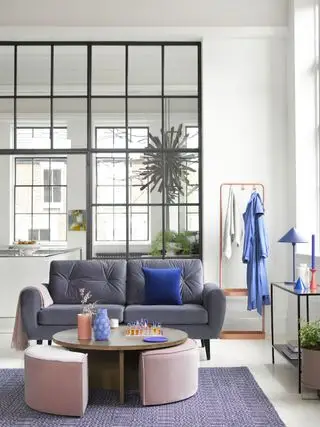 sala de estar em plano aberto com janelas abertas dividindo o espaço, tapete roxo e pufes rosa