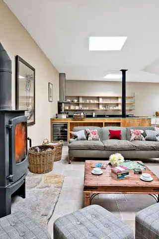 salon moderne ouvert avec petite cuisine derrière avec sol en pierre et poêle à bois