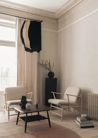 sala de estar neutra con dos sillones de madera, una pequeña mesa de centro cuadrada de madera oscura, alfombra, cortinas negras y de piedra, detalles en negro