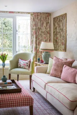 salón rosa y verde, con cortinas florales, sofá y cojines verdes y rosas, sillón verde, lámpara de pantalla plisada