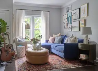 sala de estar gris pálido con sección azul, taburete de cuero, alfombra vintage y pared de galería