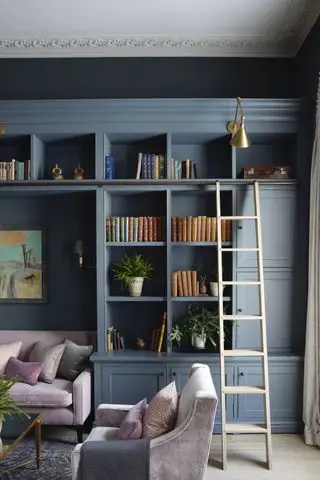 Hjemmebibliotek med blå hyller og stige, sofa og lenestol