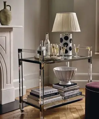Carrello porta bevande in metallo e vetro, decorato con lampada da tavolo, bicchieri, libri e soprammobili