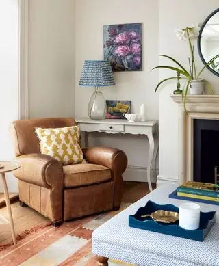 Una poltrona in pelle marrone con cuscino giallo, lampada blu e pouf blu.