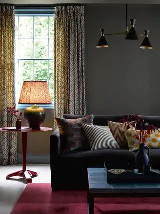 illuminazione a strati in uno studio accogliente con divano di velluto scuro ricoperto di cuscini e tappeto rosso