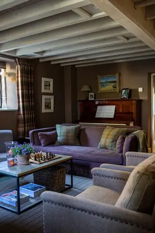 accogliente e accogliente soggiorno con divano viola, poltrone color crema e soffitto con travi a vista