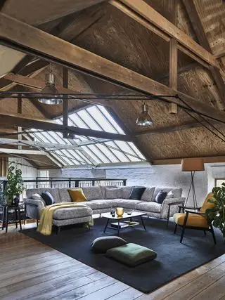 sala de estar loft com teto abobadado, seção cinza sobre tapete azul, poltronas, luzes pendentes