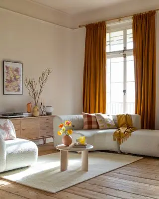 sala de estar neutra com toques de laranja, corte boule creme, tapete, aparador retrô, pequena mesa de centro