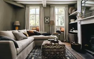 sala de estar verde e neutra com tapete e pufe seccional e estampado, sanefas, estantes abertas, piso de madeira, lareira