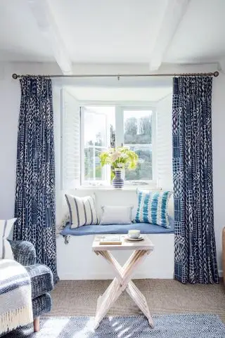 Détail du salon avec table pliante devant la fenêtre et rideaux bleus et blancs