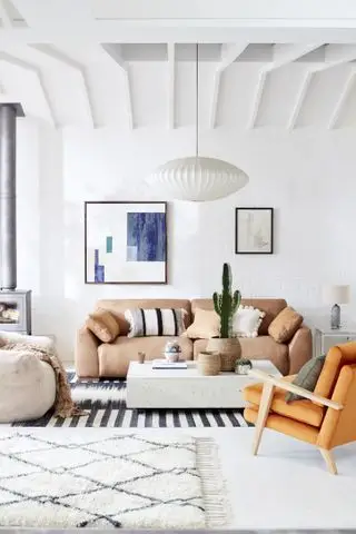 salón blanco con vigas, sofá, sillón y alfombras, cuadros en la pared