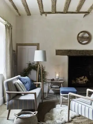 Salón de estilo rústico con vigas y chimenea, sofá, sillón y alfombra.