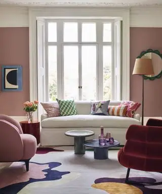 Ein rosa gestrichenes Wohnzimmer mit weißem Sofa und buntem Sessel und Accessoires.
