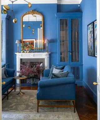 Azurblau gestrichenes Wohnzimmer mit passenden Doppelsofas, weißem Kamin, Metallspiegel und Pendelleuchte