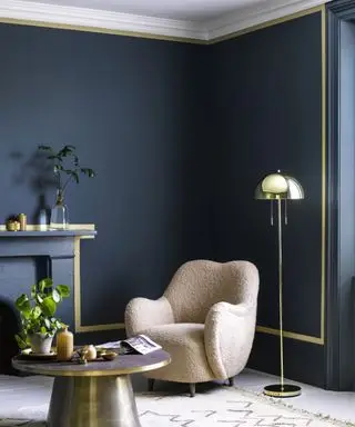 Blau gestrichenes Wohnzimmer mit gelbem Akzentstreifen, cremefarbenem Loungesessel mit metallischer Stehlampe und Couchtisch