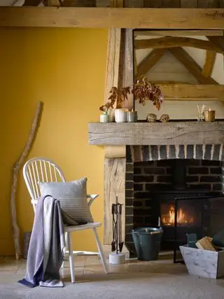 Gelbes Wohnzimmer mit Holzofen, Balken, Spindelstuhl, rustikalen Möbeln, Landhausstil, Steinboden
