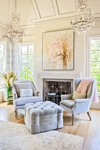 sala de estar creme com teto apainelado, poltronas cinza e escabelo, lareira e lustre