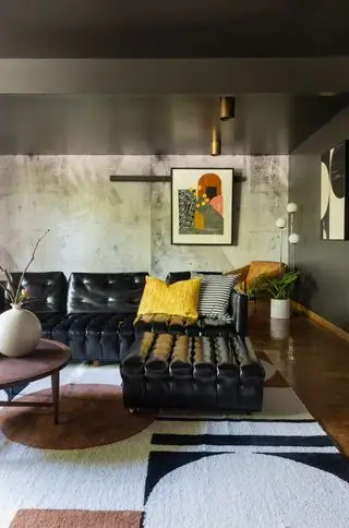 sala de estar moderna com sofá de couro, tapete monocromático geométrico, teto baixo e parede em estilo cimento
