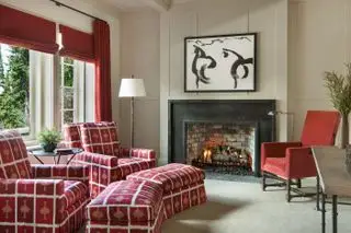 Sala de estar vermelha com lareira, poltronas com estofamento estampado vermelho e estofamento vermelho liso, persianas e cortinas vermelhas e paredes e piso neutros