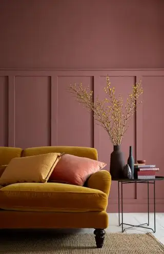 Sala com sofá amarelo, mesa lateral, painéis e superior pintado em marrom vermelho