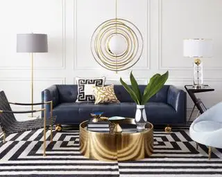 Gullbelysning og aksenter sammen med en marineblå Jonathan Adler Claridge-sofa som illustrerer hvordan man planlegger stuebelysning.