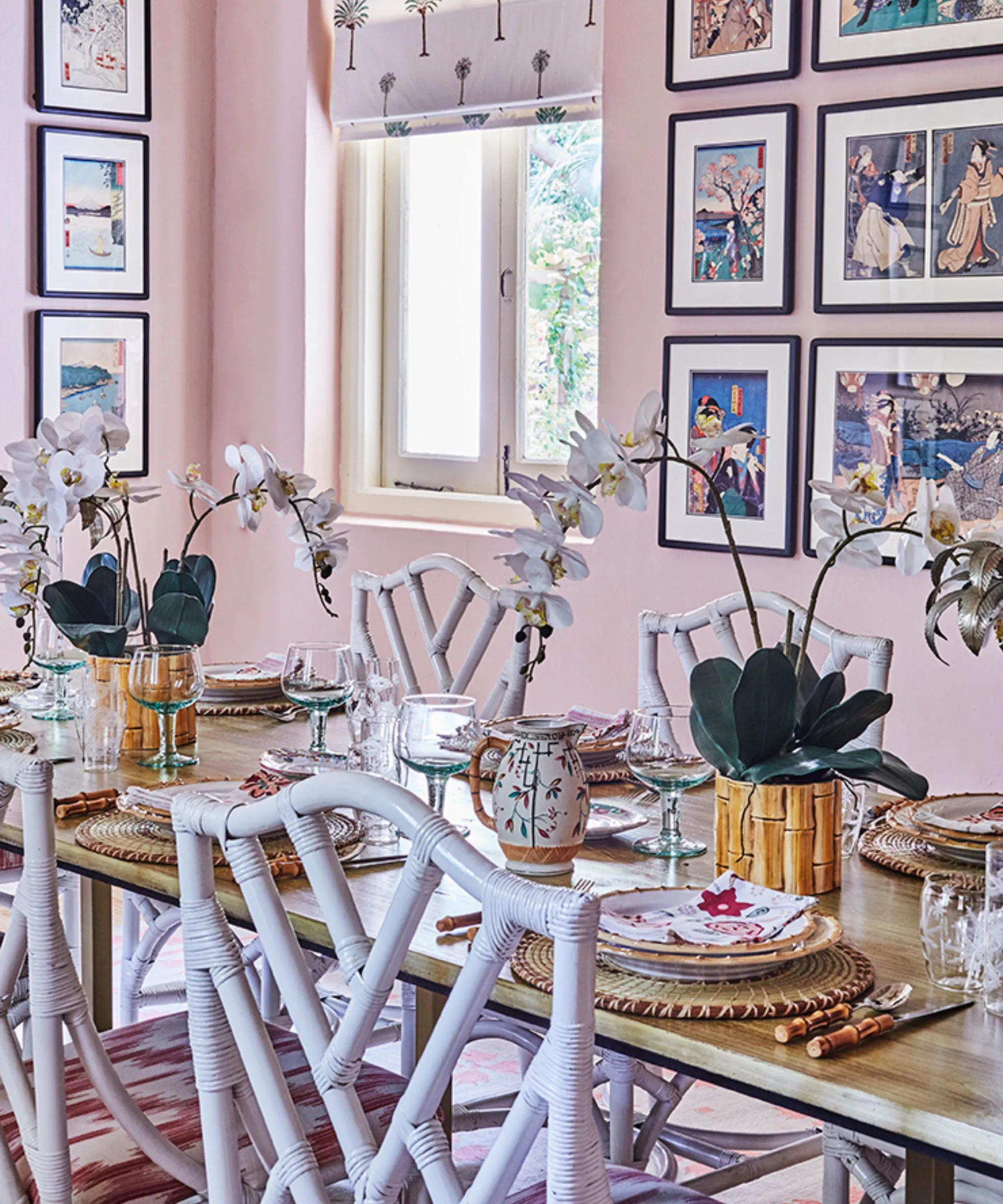 Comedor rosa con sillas de mimbre blancas, mesa de madera y platos de ratán' loading='lazy' title=
