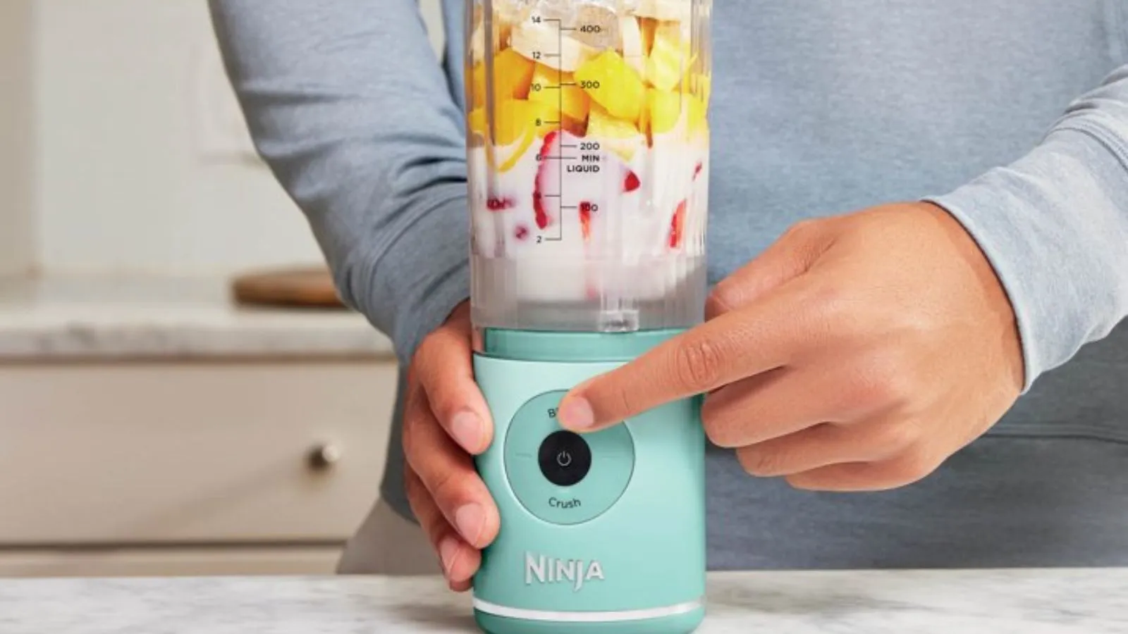 En mann slår på den mintfargede Ninja Blast Max-blenderen fylt med tropiske ingredienser' loading='lazy' title=