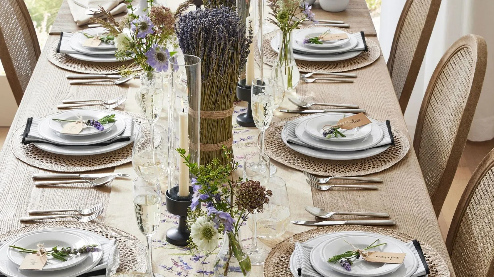 Table à manger en bois avec vaisselle blanche, sets de table en rotin, gros bouquets de lavande et vases à bourgeons en verre' loading='lazy' title=